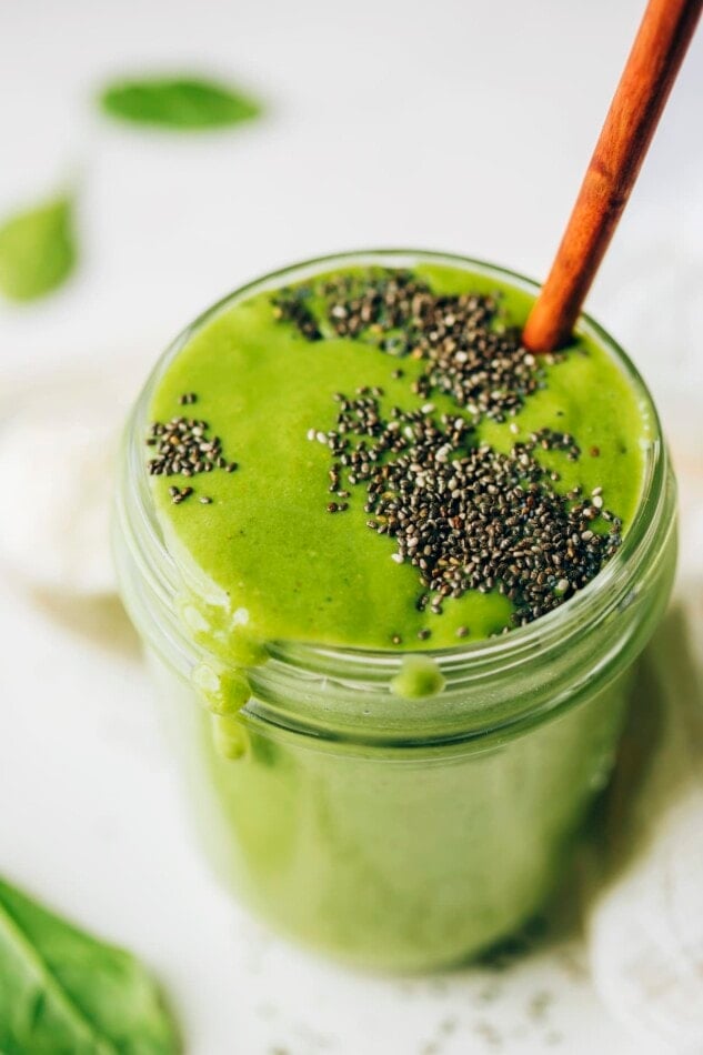 A mason jar containing green protein smoothie, topped with black chia seeds. A wooden straw sticks out of the top of the smoothie.