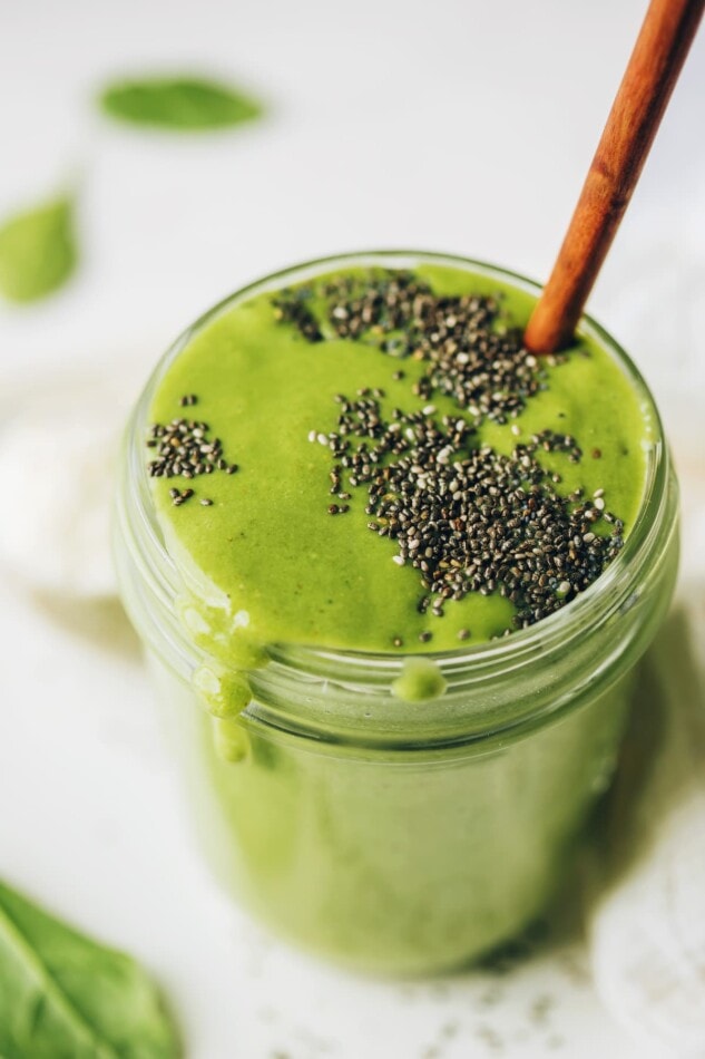 A mason jar containing green protein smoothie, topped with black chia seeds. A wooden straw sticks out of the top of the smoothie.