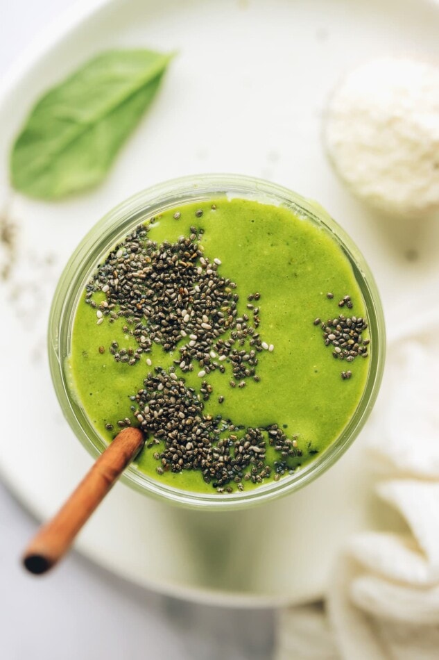 An overhead photo looking at a mason jar containing green protein smoothie that has been topped with black chia seeds. A straw sticks out of the mason jar.