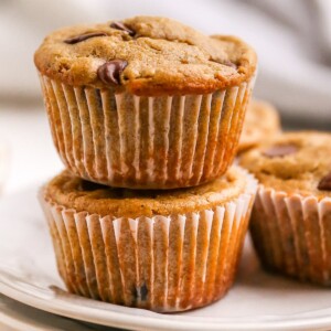 Two healthy chocolate chip muffins stacked on top of each other. They are wrapped in a paper liner.