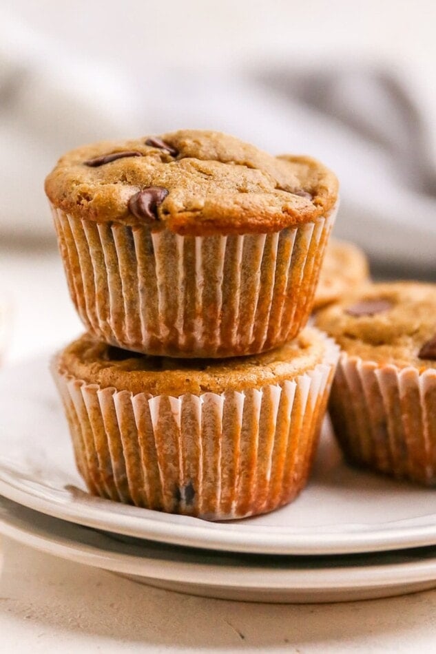 Two healthy chocolate chip muffins stacked on top of each other. They are wrapped in a paper liner.