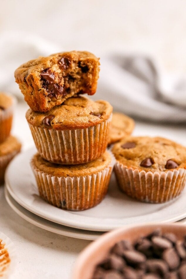 Muffins on a plate. Three are stacked on top of each other, the top muffin has no paper liner and a bite taken out of it. There is an additional muffin on the plate next to the stack.