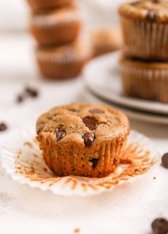 A chocolate chip muffin unwrapped from its paper liner, resting on the paper liner.