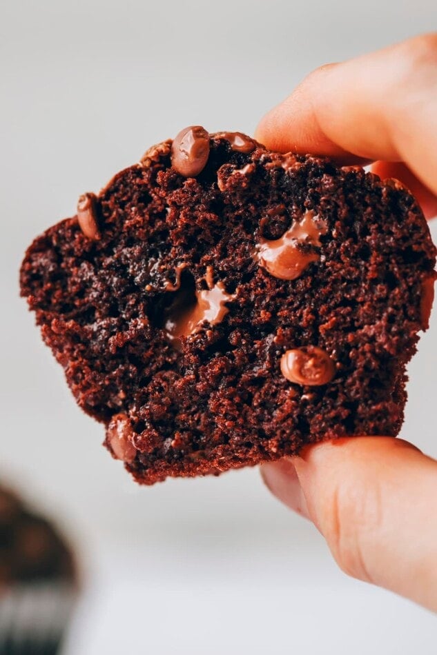 A healthy chocolate chip muffin cut in half. A hand is holding up the half so you can see the gooey chocolate chips inside.
