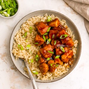 An overhead photo of a bowl of rice with healthy orange chicken. A fork rests in the rice.