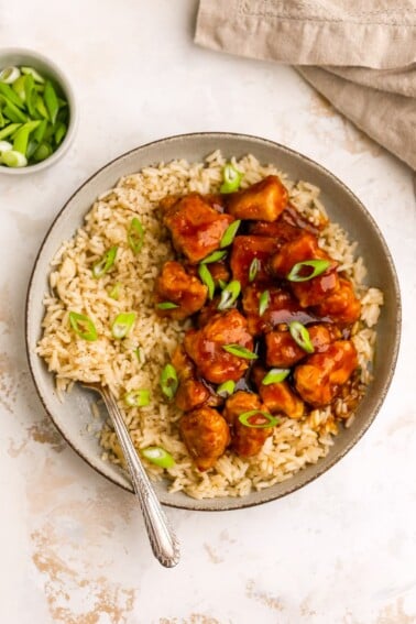 An overhead photo of a bowl of rice with healthy orange chicken. A fork rests in the rice.