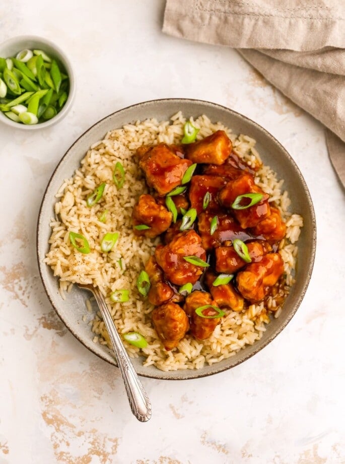 An overhead photo of a bowl of rice with healthy orange chicken. A fork rests in the rice.