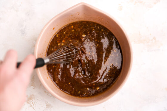 Tamari, rice vinegar, sesame oil, water, arrowroot powder, orange juice, orange zest, garlic, fresh ginger, honey, sea salt, black pepper in a bowl being whisked together.