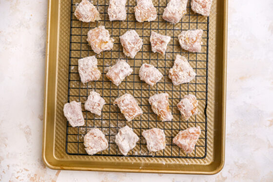 Pieces of chicken on a wire rack on top of a baking sheet after being dipped into egg and then flour mixture.