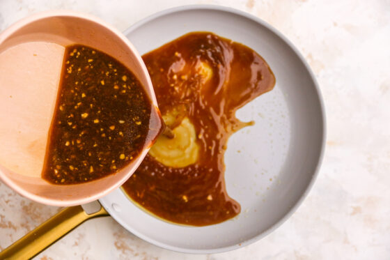 Pouring orange chicken sauce into a skillet to warm it up.