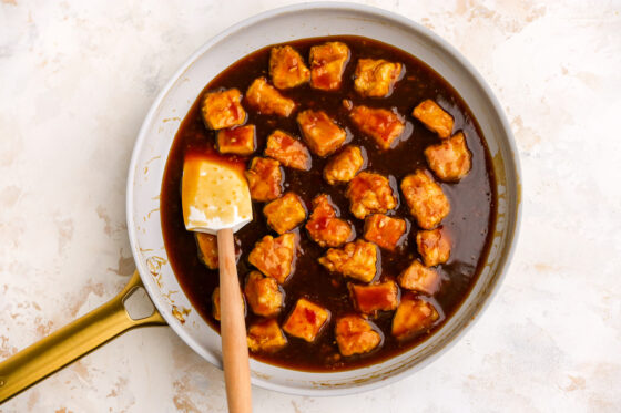 Chicken tossed in orange sauce in a skillet.