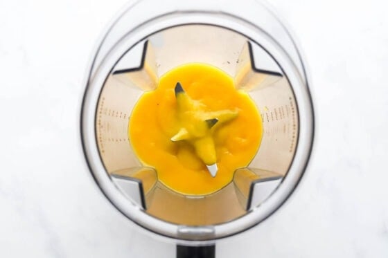 A high powered blender with mango blended into a puree.