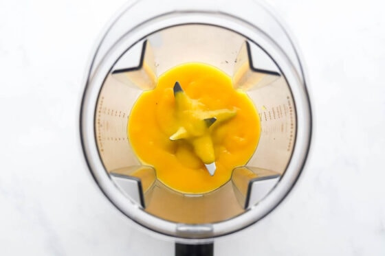 A high powered blender with mango blended into a puree.