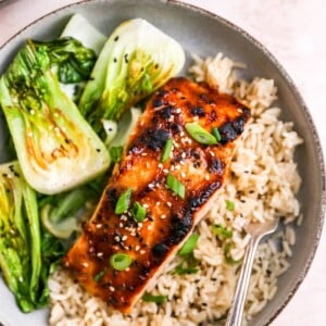 A close up of a miso salmon filet over a bed of rice next to some bok choy.