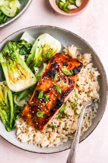 A close up of a miso salmon filet over a bed of rice next to some bok choy.