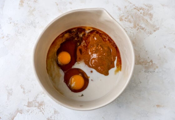 A mixing bowl containing almond butter, eggs, maple syrup, almond milk and vanilla extract.
