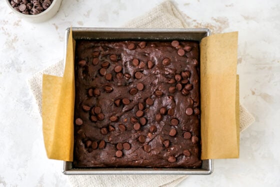 Freshly baked protein brownies in an 8x8 baking pan lined in brown parchment paper.