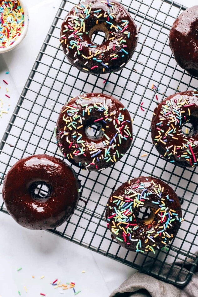 An overhead view of a wire cooling rack with protein donuts coated in chocolate and toped with sprinkles.