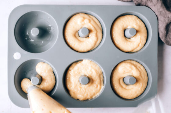 Donut batter being piped into a 6 donut cavity pan.