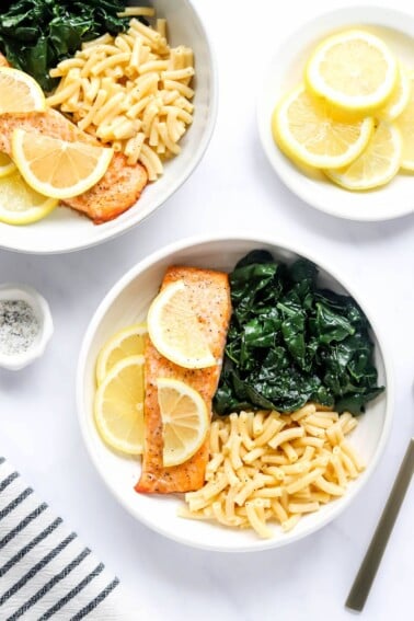 An overhead photo of a bowl with macaroni and cheese, kale and a filet of salmon. Lemon slices top the salmon filet.