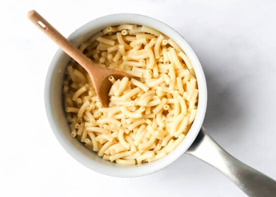 Boxed macaroni and cheese prepared in a sauce pot. A wooden spoon rests in the bowl.