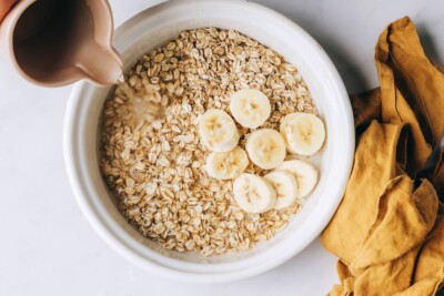 A bowl containing oats, banana slices and salt. Hot water is being poured into the bowl.