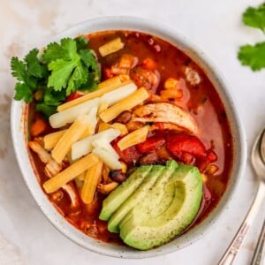 A bowl of chicken enchilada soup, topped with shredded cheese, avocado slices and fresh cilantro.