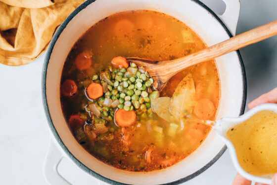 Vegetable broth being added to large pot.