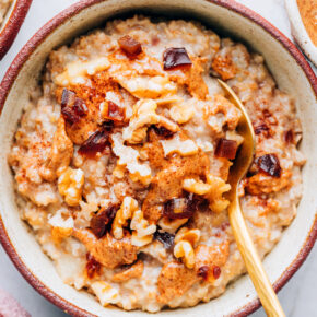 A bowl containing salted date nut oatmeal. The oatmeal is topped with walnuts and an almond butter drizzle. A spoon rests in the bowl.