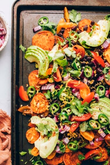 Sweet potato nachos topped with fresh avocado slices, jalapeño slices, and freshly chopped cilantro on a sheet pan.