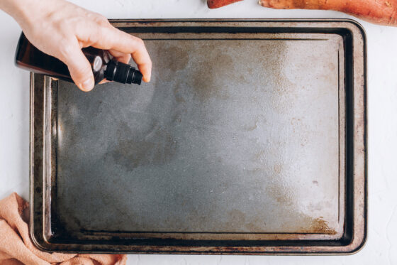 A sheet pan being sprayed with oil.