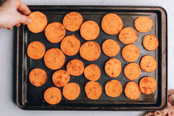 Seasoned sweet potato rounds evenly distributed on the prepared sheet pan.