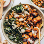 A vegan power bowl drizzled with creamy white bean dressing. A gold fork rests in the bowl.