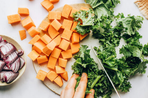 Chopping kale and sweet potatoes. A bowl of chopped red onion is nearby.