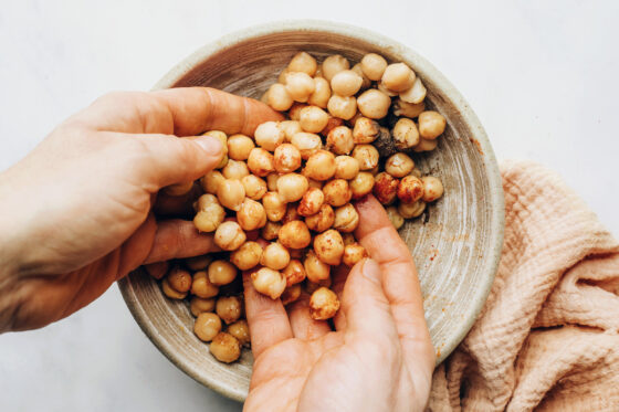 Two hands are coating chickpeas in a bowl with brown sugar, chili powder, salt and pepper.
