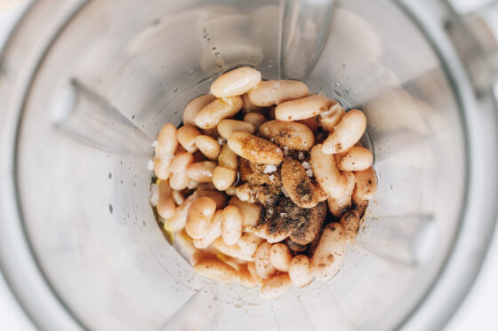 A high powered blender containing cannellini beans, water, apple cider vinegar, olive oil, salt, pepper and cumin.