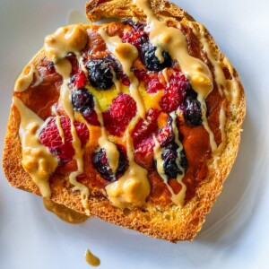 Yogurt toast on a white plate with blueberries and raspberries and a drizzle of nut butter.