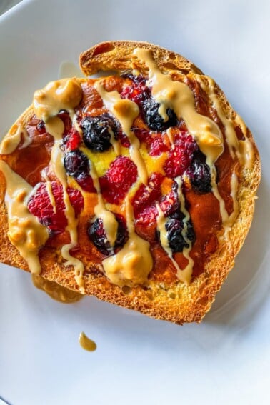 Yogurt toast on a white plate with blueberries and raspberries and a drizzle of nut butter.