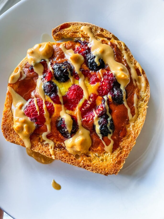 Yogurt toast on a white plate with blueberries and raspberries and a drizzle of nut butter.