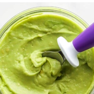 A small jar of avocado puree. A spoon rests in the jar.