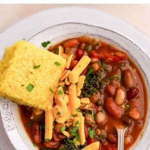 Bowl of bean soup topped with shredded cheddar and a slab of cornbread.