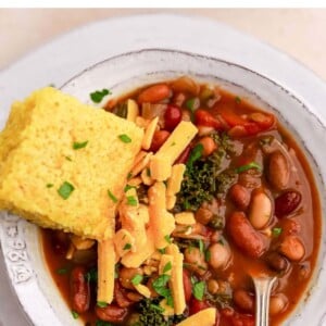 Bowl of bean soup topped with shredded cheddar and a slab of cornbread.