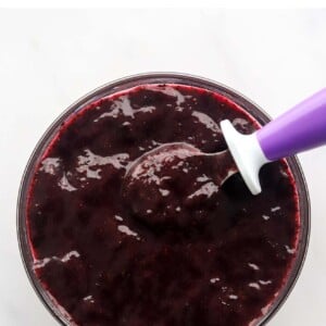 A bowl of blueberry puree with a purple spoon resting in the bowl.
