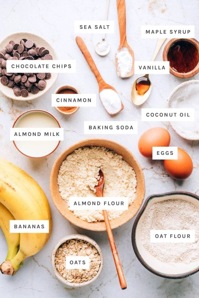 Ingredients measured out to make oatmeal banana muffins: chocolate chips, sea salt, maple syrup, vanilla, cinnamon, baking soda, coconut oil, almond milk, eggs, almond flour, bananas, oats, oat flour.