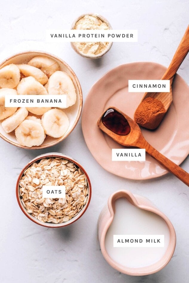 Ingredients measured out to make an oatmeal smoothie: vanilla protein powder, frozen banana, cinnamon, vanilla, oats and almond milk.