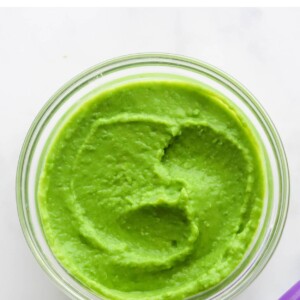 A small jar of pea puree. A purple spoon is cut out of the frame.