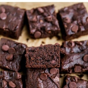 Squares of brownies on a sheet of brown parchment paper. The center brownie is resting against another brownie, exposing the inside.