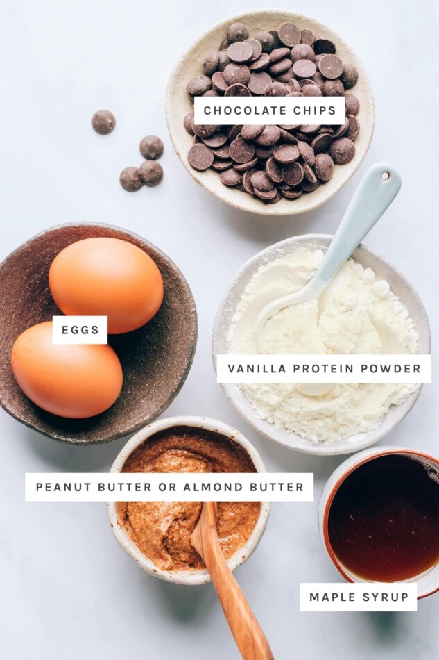 Ingredients measured out to make protein cookies: chocolate chips, eggs, vanilla protein powder, peanut butter/almond butter and maple syrup.