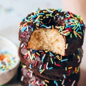 Stack of three protein donuts, frosted with chocolate icing and decorated with sprinkles. A bite is taken out of the top donut.