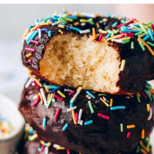 Stack of three protein donuts, frosted with chocolate icing and decorated with sprinkles. A bite is taken out of the top donut.